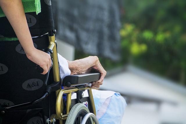 若い人が高齢者の車いすを押して外出を介助している。